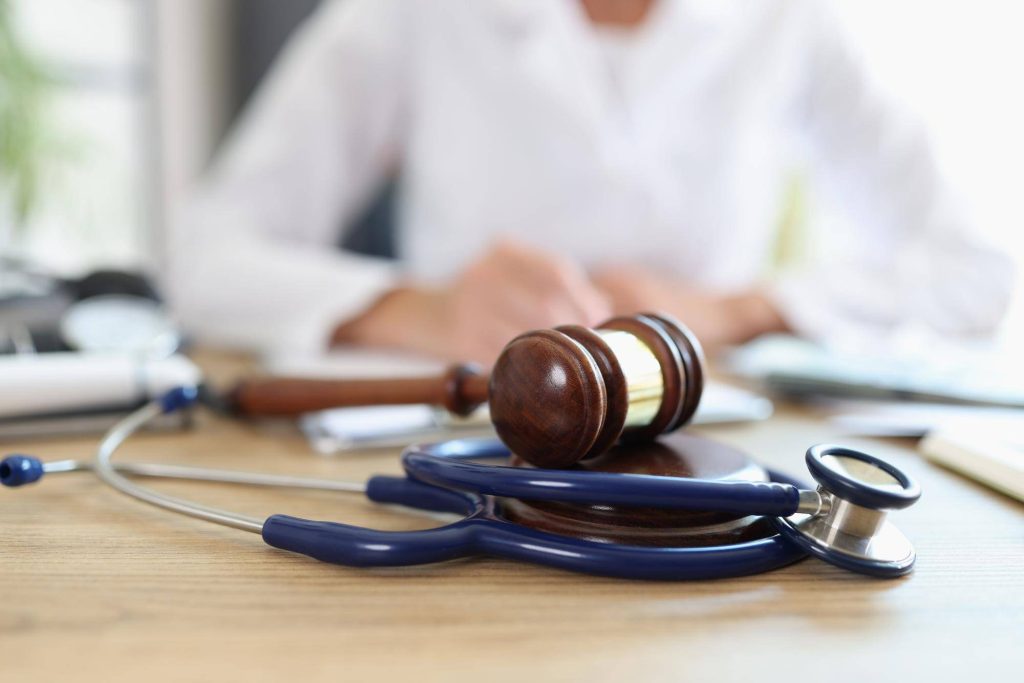 Un mazo de madera y un estetoscopio azul sobre un escritorio de madera en un consultorio médico, representando las opciones legales de Demandar-a-un-hospital-público-y-a-una-clínica-privada.