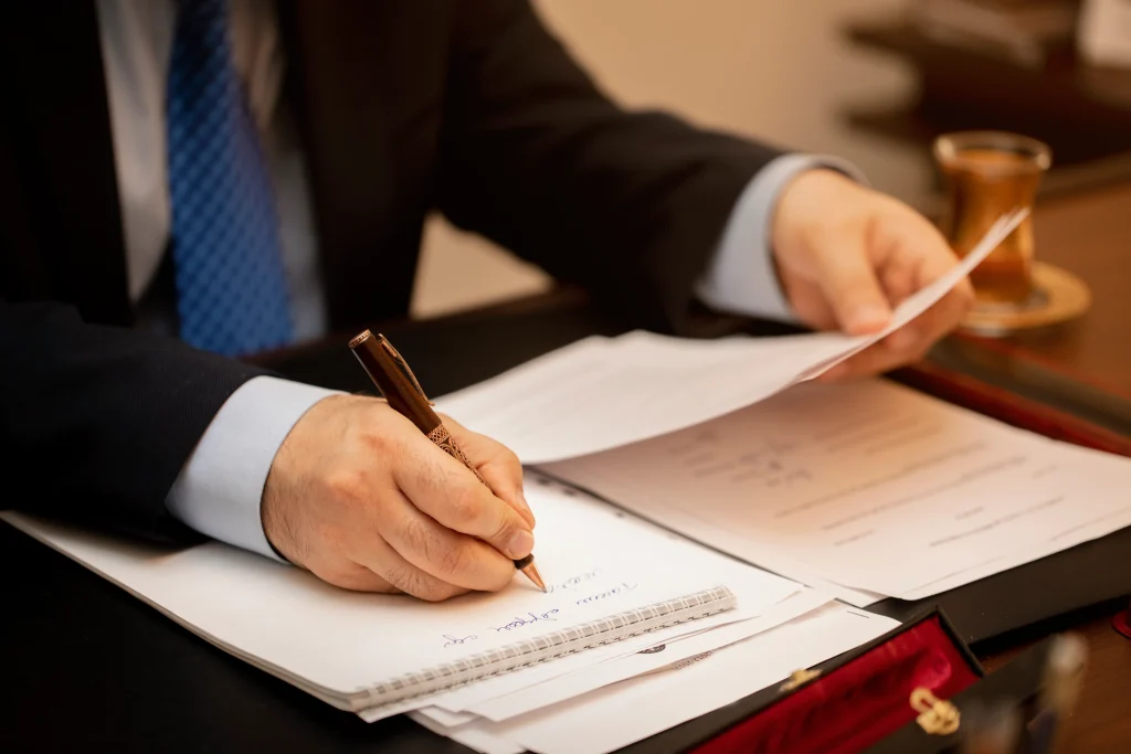Primer plano de un profesional en traje revisando y tomando notas sobre documentos legales en un escritorio, representando la labor de un abogado experto en negligencias médicas.